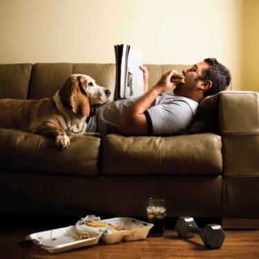 Man eating and lying on couch with dog